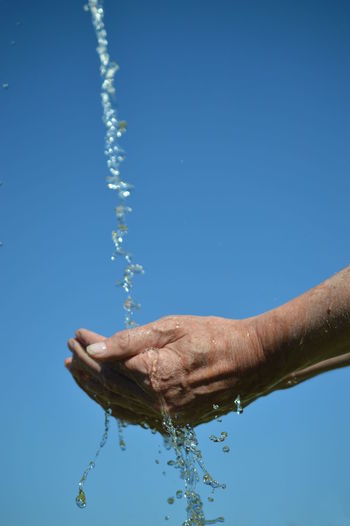 Cropped image of person washing hands against clear blue sky