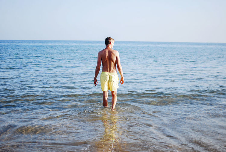 Rear view of man in yellow swim suit standing in sea against sky