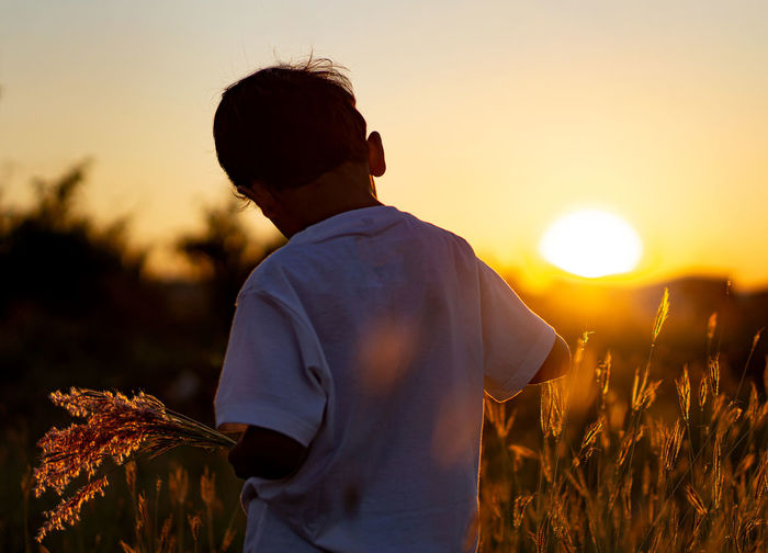Rear view of boy standing against sky during sunset