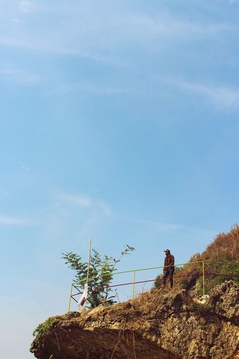 Low angle view of teenage boy standing on cliff against sky