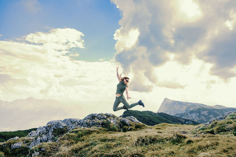Happy woman jumping on mountain against cloudy sky