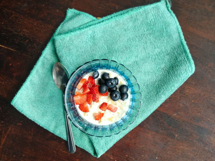Cooked oat with forest fruits. strawberries and blueberries in a blue glass bowl on a green napkin.
