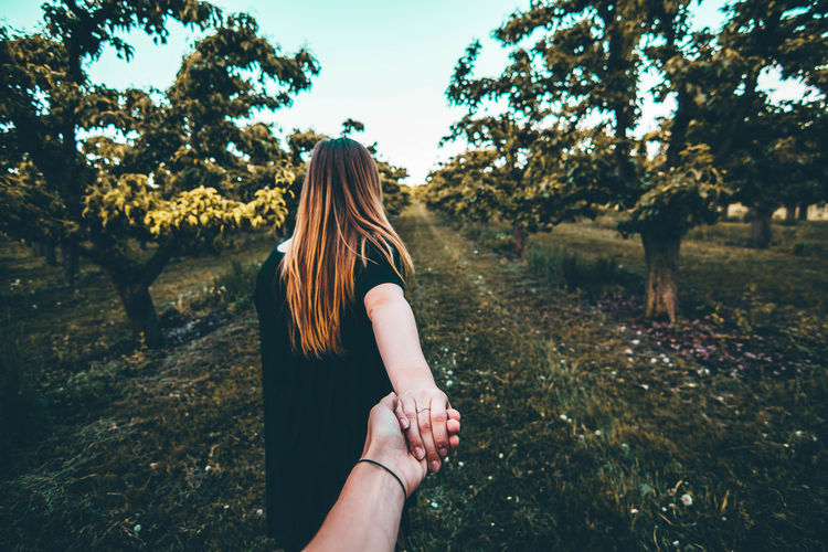 Cropped hand of man holding girlfriend hand on grassy field