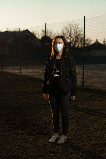 Full length of woman wearing mask standing on land at sunset