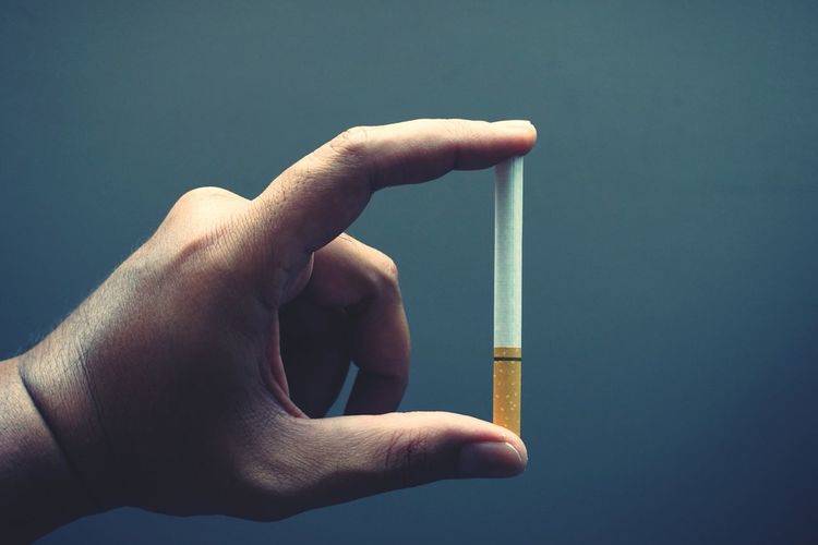 Cropped hand holding cigarette against gray background