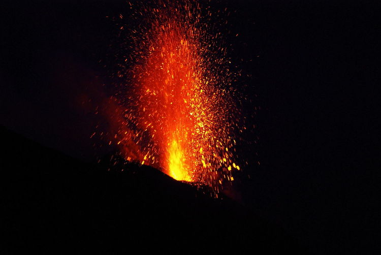 Low angle view of lava erupting at silhouette mountain