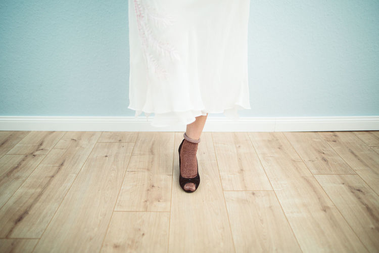 Low section of woman wearing high heels while standing on hardwood floor