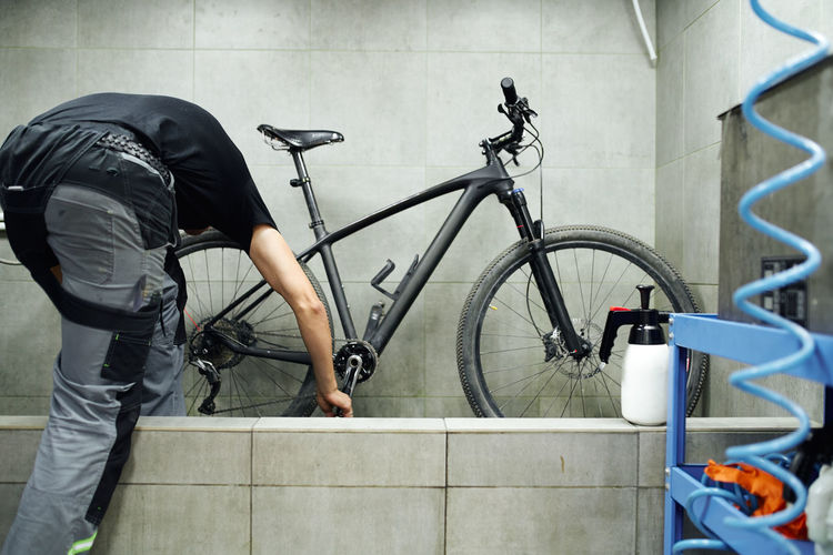 Unrecognizable male mechanic cleaning gear cassette of bicycle wheel with water in workshop