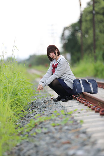 Portrait of young woman in school uniform sitting on railroad track