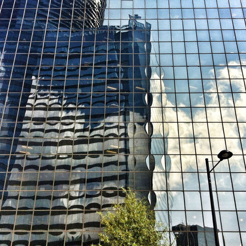 Low angle view of modern glass building in city against sky