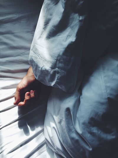 Person's hand covered with blanket on bed