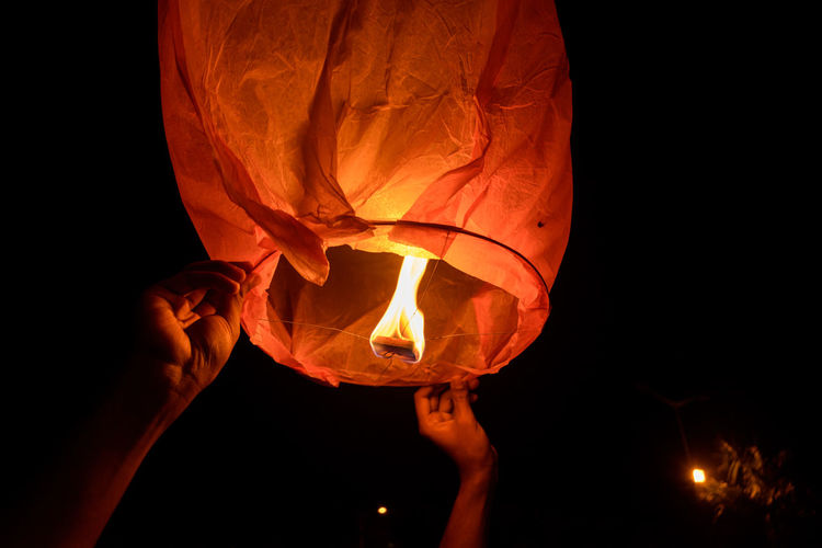Close-up of hand holding illuminated lantern against sky at night