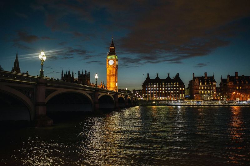 Illuminated big ben with westminster bridge over thames river against sky at night
