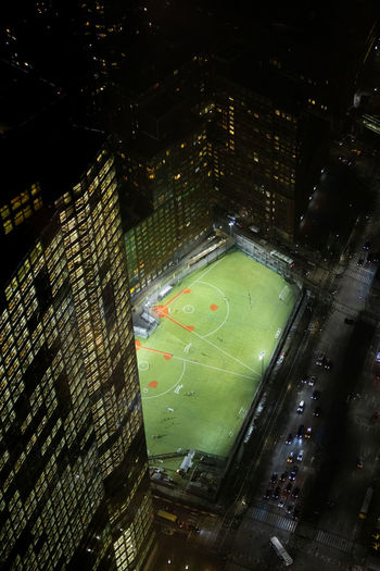 From above of green baseball field with white lines located near modern building on night time in new york city