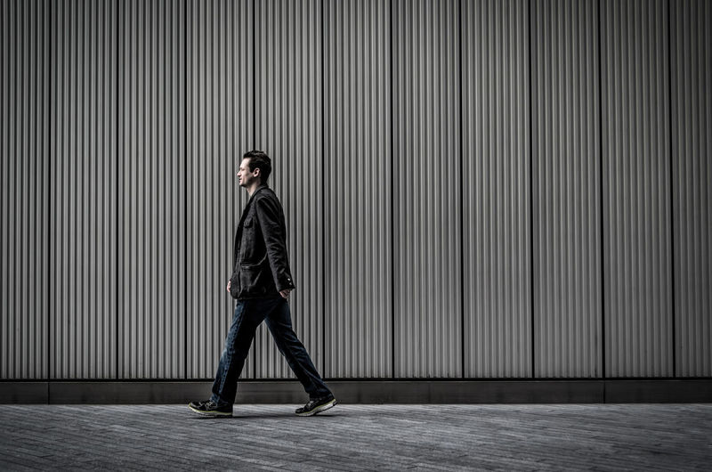 Side view of man walking on sidewalk by wall