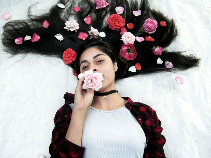 High angle portrait of young woman with flowers lying on bed