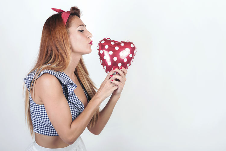 Portrait of young woman holding heart shape over white background