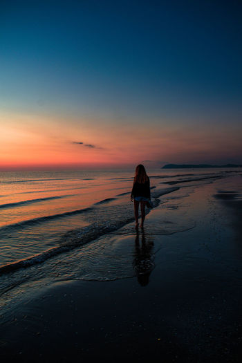 Rear view of silhouette man walking on beach during sunset