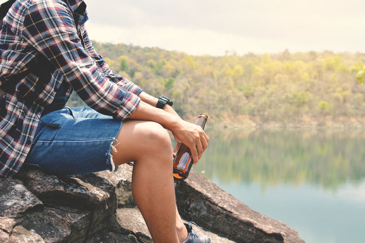 Close-up of man sitting on rock by river against sky