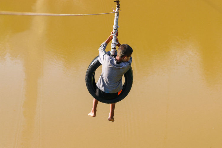 Rear view full length of boy hanging from tire over lake