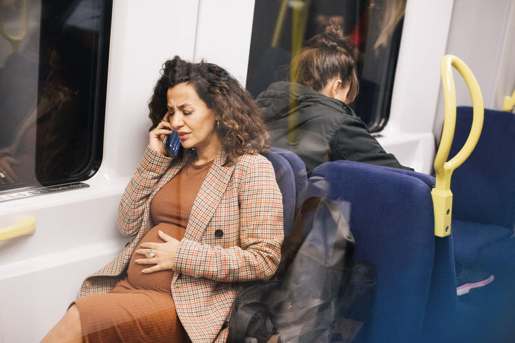 Pregnant businesswoman talking on smart phone while sitting in train