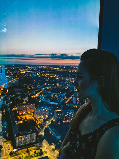 Portrait of woman looking at illuminated city buildings against sky