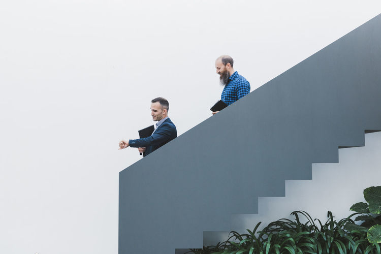 Side view of male coworkers walking downstairs in creative workplace with green plants