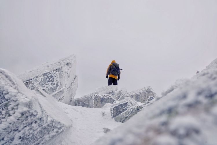 Low angle view of mid adult man with backpack standing on snowcapped mountain against sky