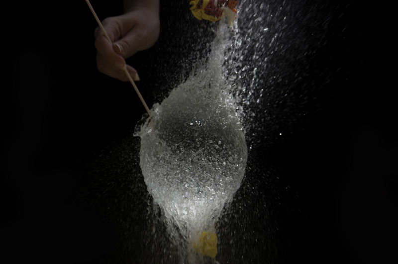 Close-up of hand bursting water bomb against black background