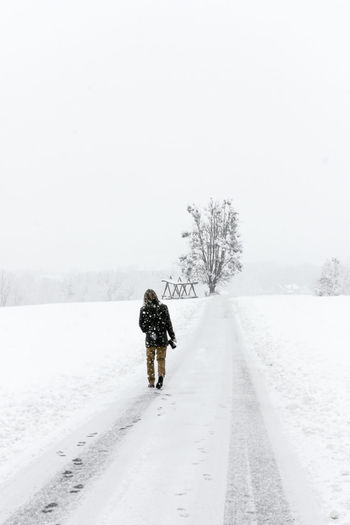 Rear view of man walking on snow covered field