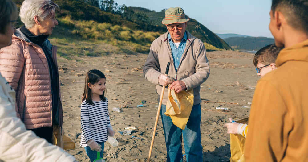 Grandparents and grandchildren cleaning while standing at beach