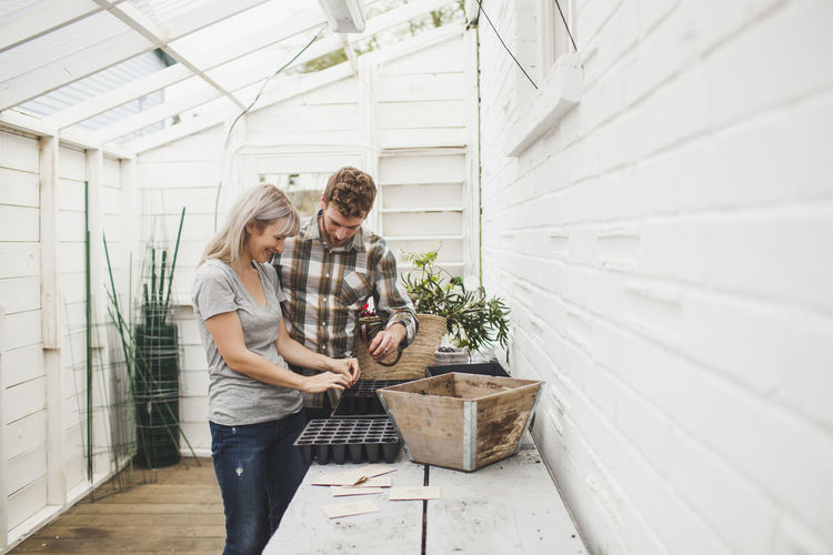 Couple pouring seeds in seedling tray while standing in greenhouse