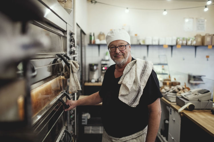Portrait of senior baker standing by oven at bakery