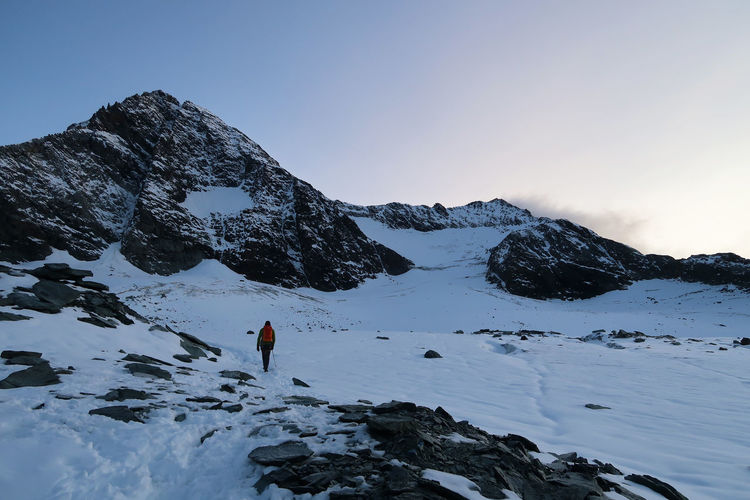 Man hiking on snowcapped mountain against clear sky
