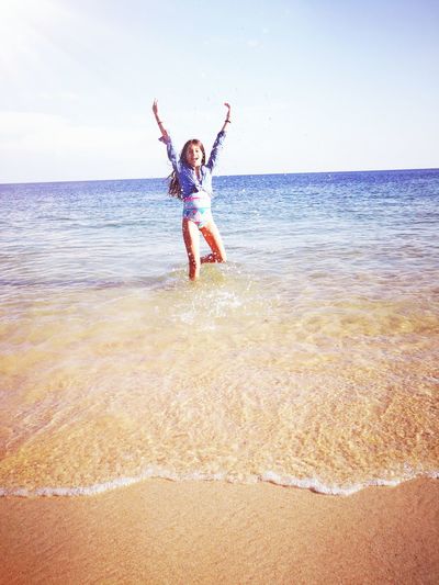 Portrait of happy girl with arms raised standing in sea against sky