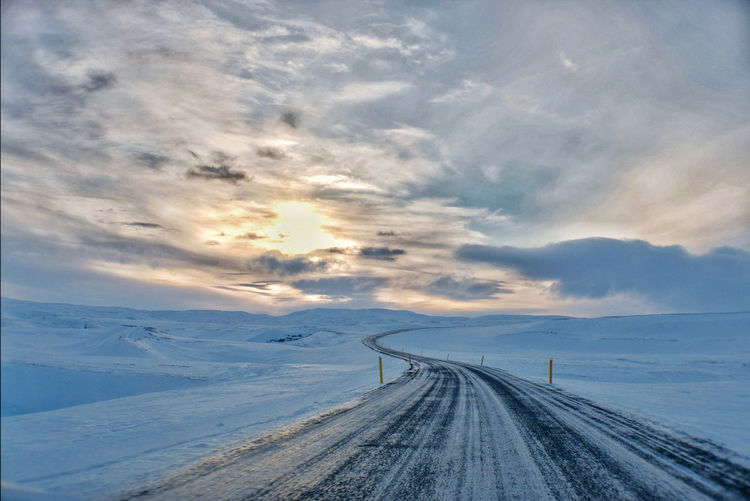 Road leading towards snow covered landscape against sky