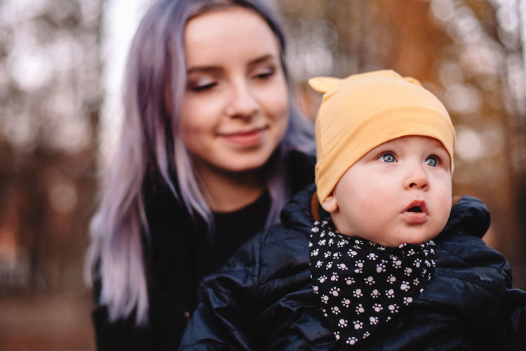 Young mother holding baby boy while sitting in park during autumn