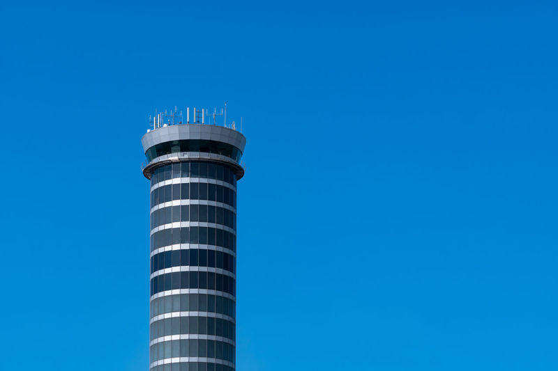 Air traffic control tower in the airport with international flight plane flying on clear blue sky. 