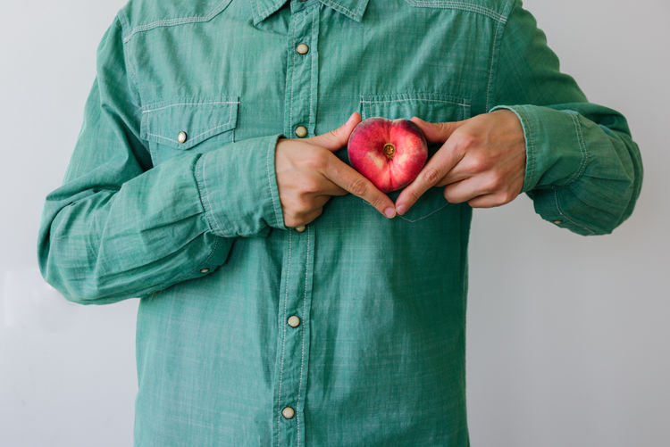 Midsection of man holding peach against white background