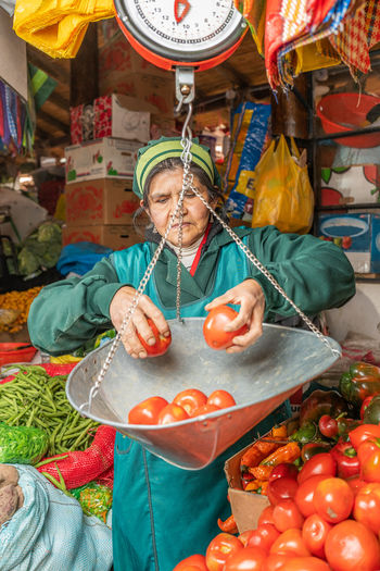 Focused peruvian female seller weighing tomatoes on scales while selling on itinerant fair in city of cusco