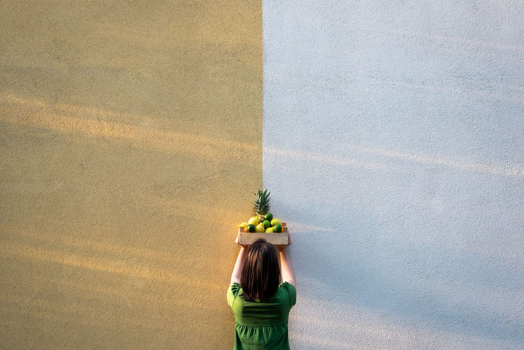 Rear view of woman with tropical fruit  standing by wall