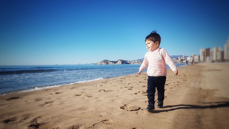 Boy standing on beach against clear blue sky