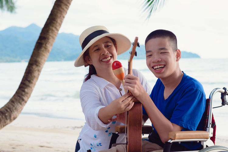 Cheerful mother holding ukulele sitting with boy at beach