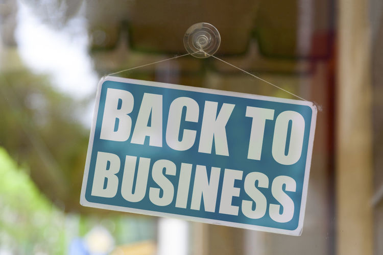 Close-up on a blue closed sign in the window of a shop displaying the message back to business.