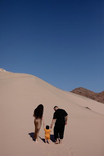 Rear view of man walking on desert against clear blue sky