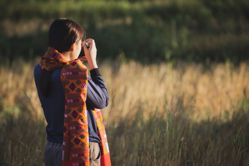 Rear view of woman photographing while standing on field