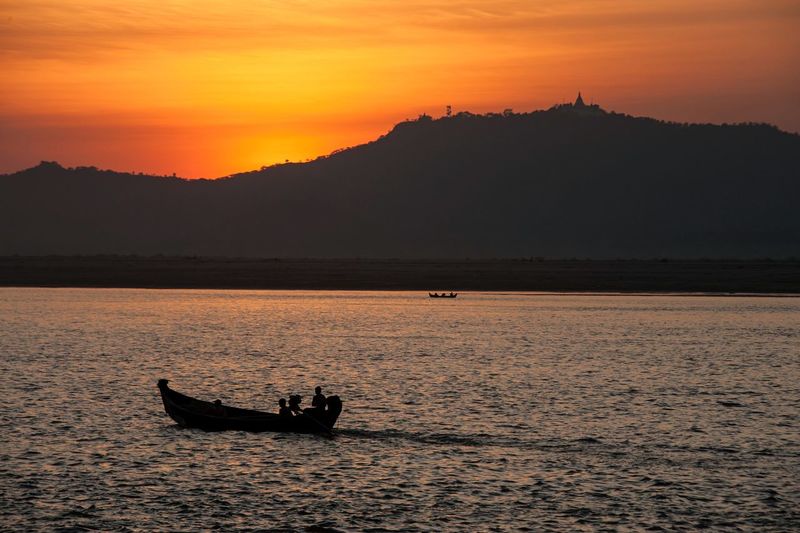 Silhouette people in boat on sea against orange sky
