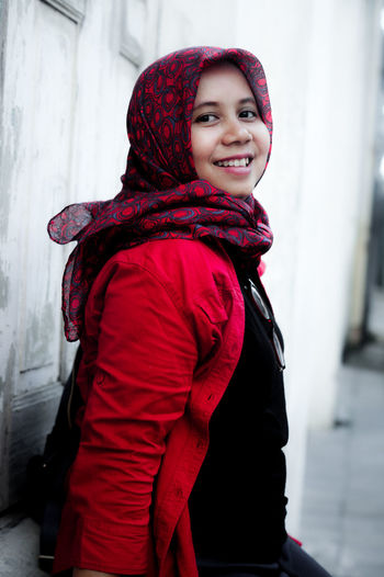 Portrait of smiling mid adult woman wearing headscarf while standing by wall