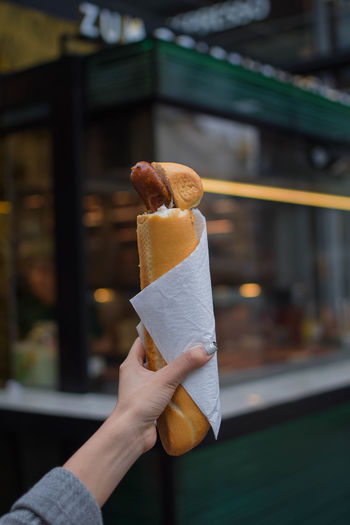 Cropped hand of woman holding hot dog against store