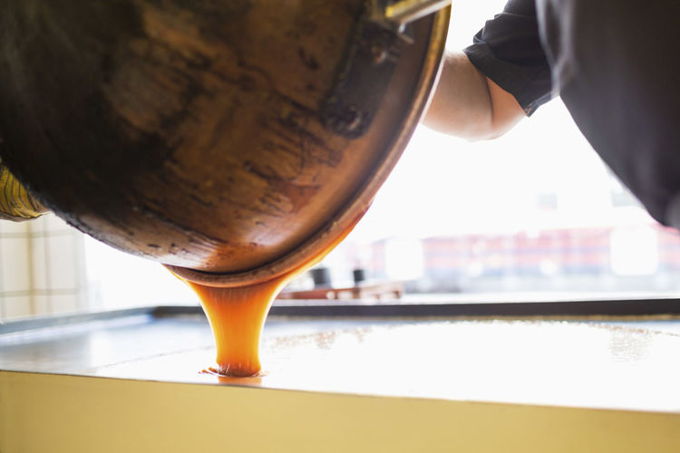 Cropped image of worker pouring caramel in container at candy store